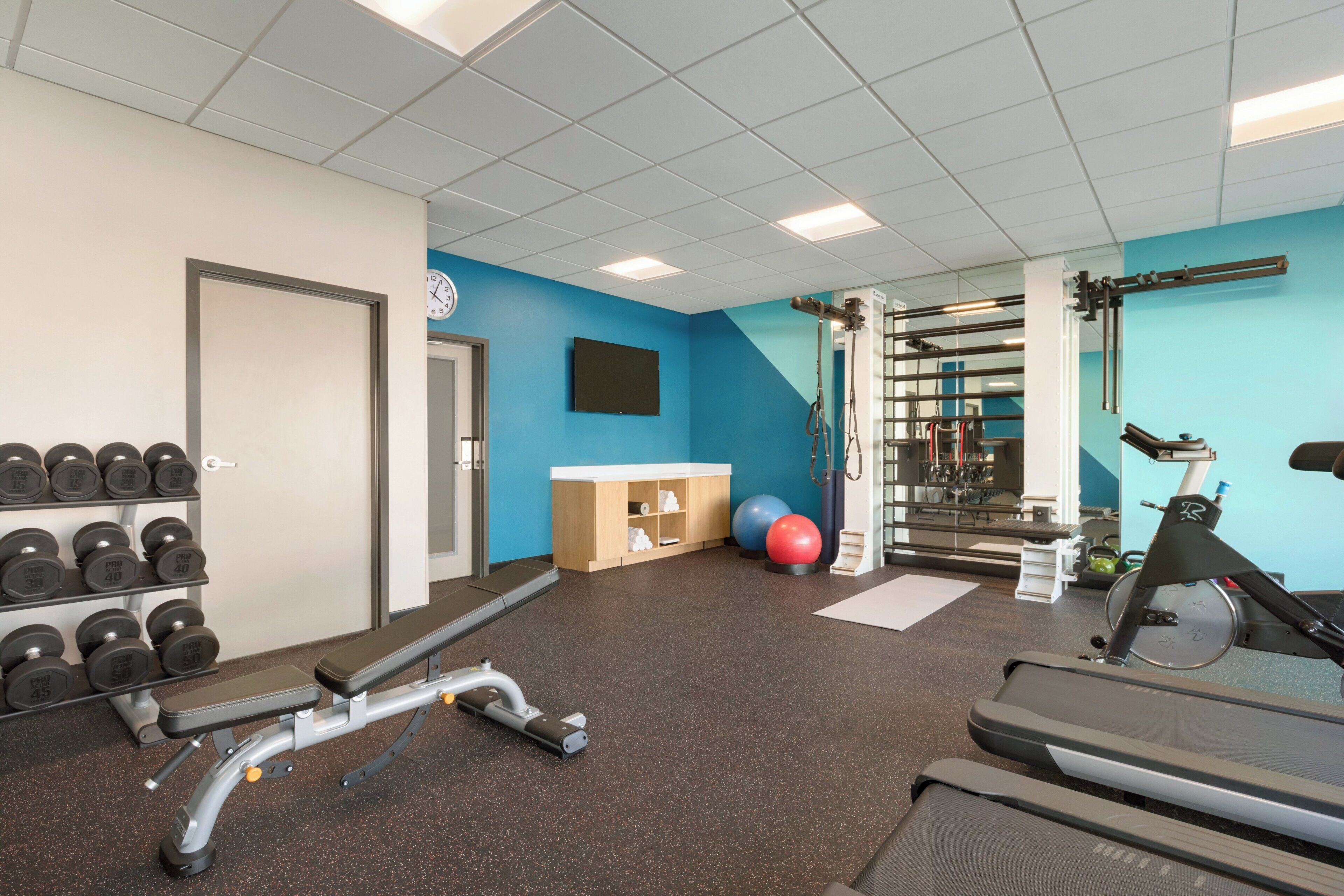 Een sportschool met trainingsapparatuur, een wandklok en een blauwe accentmuur.
