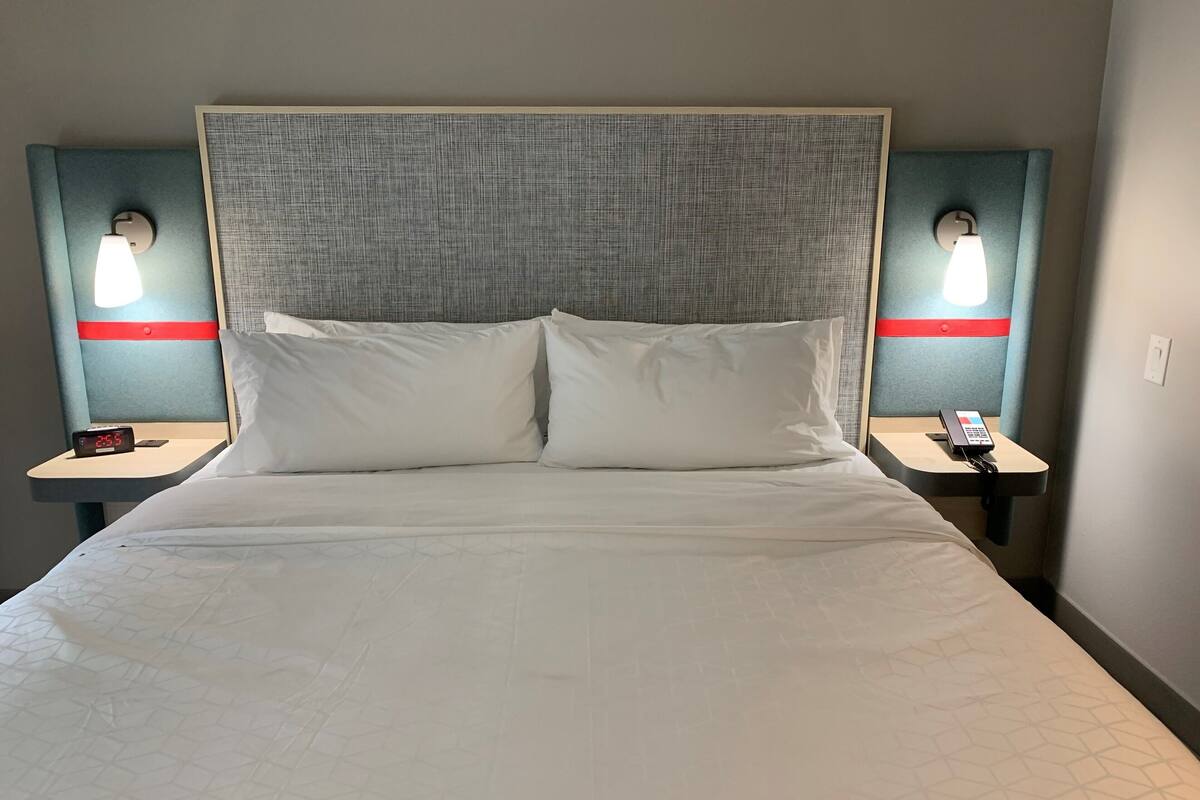 A hotel room with a large bed, two bedside tables, and two wall-mounted lamps.
