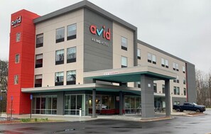 A modern hotel building with a prominent red and beige facade, a covered entrance, and a clear sign reading "avid AN IHG HOTEL". - avid hotel Salem by IHG (Salem)