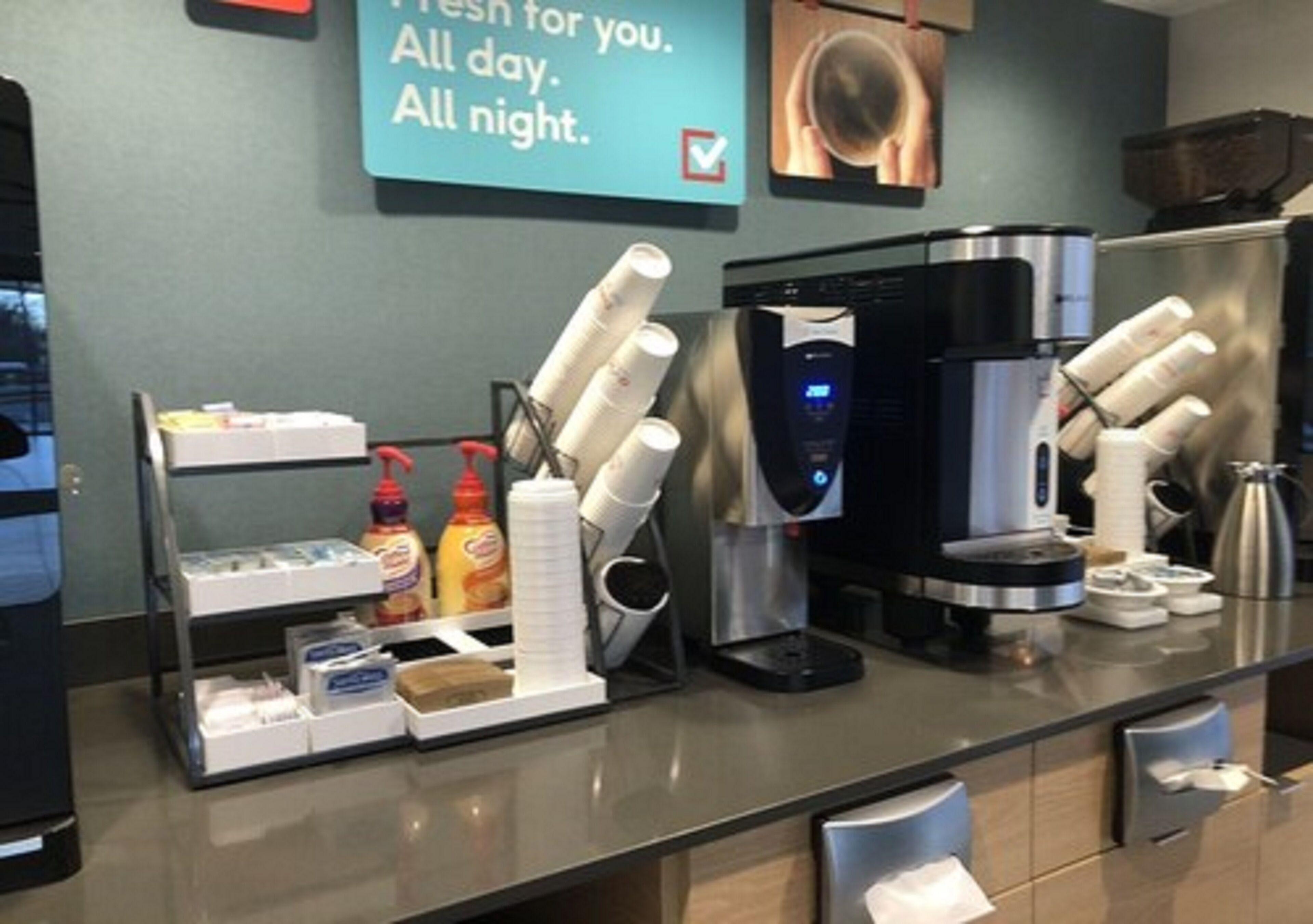 Un espace d’accueil d’hôtel équipé d’une machine à café, d’une bouilloire et d’un distributeur de café. On y trouve également des condiments et des serviettes en papier sur le comptoir.
