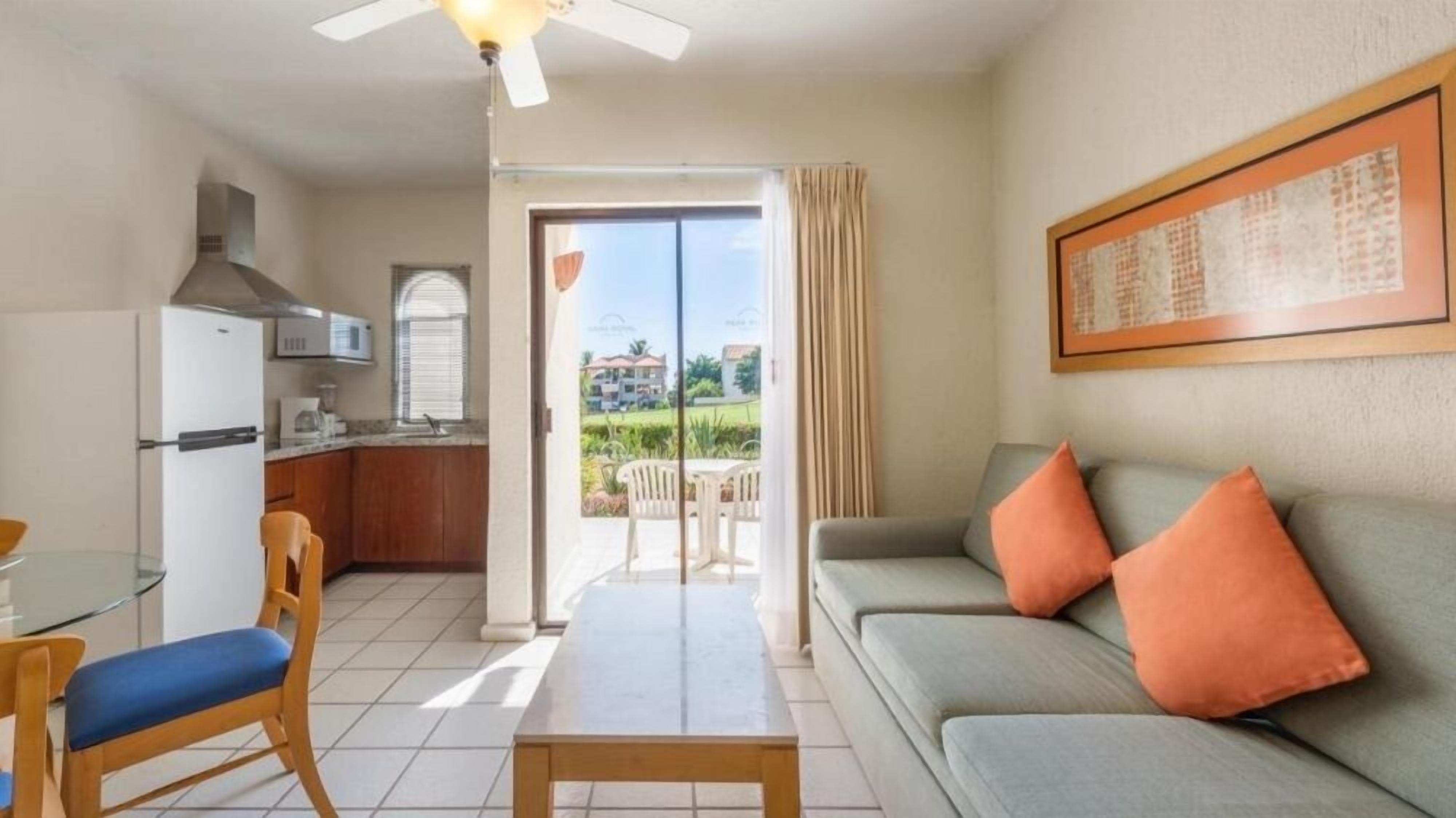 A compact living space with a kitchenette, a dining area, and a sofa with orange cushions.