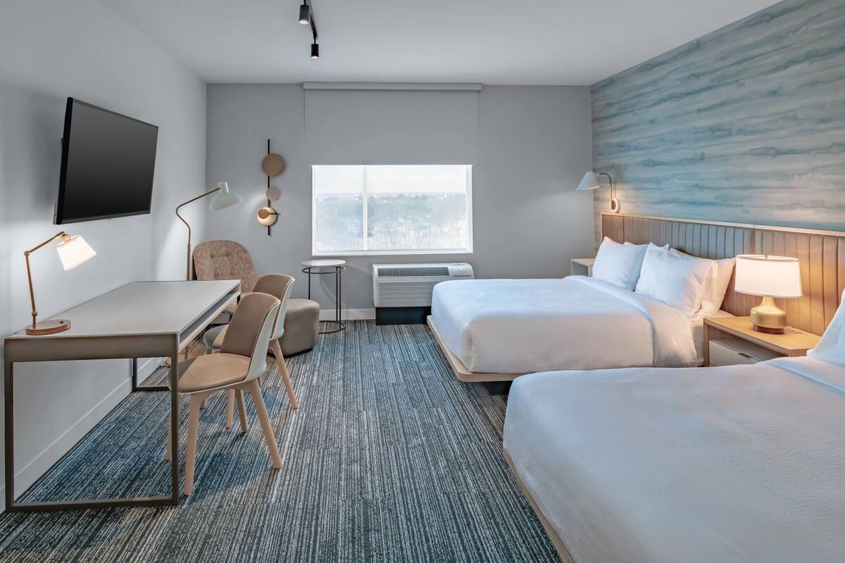 A hotel room with a bed, desk, chair, and a TV on the wall.