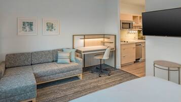 A modern, compact room with a gray sofa, a desk, a chair, a small table, and a TV mounted on the wall.