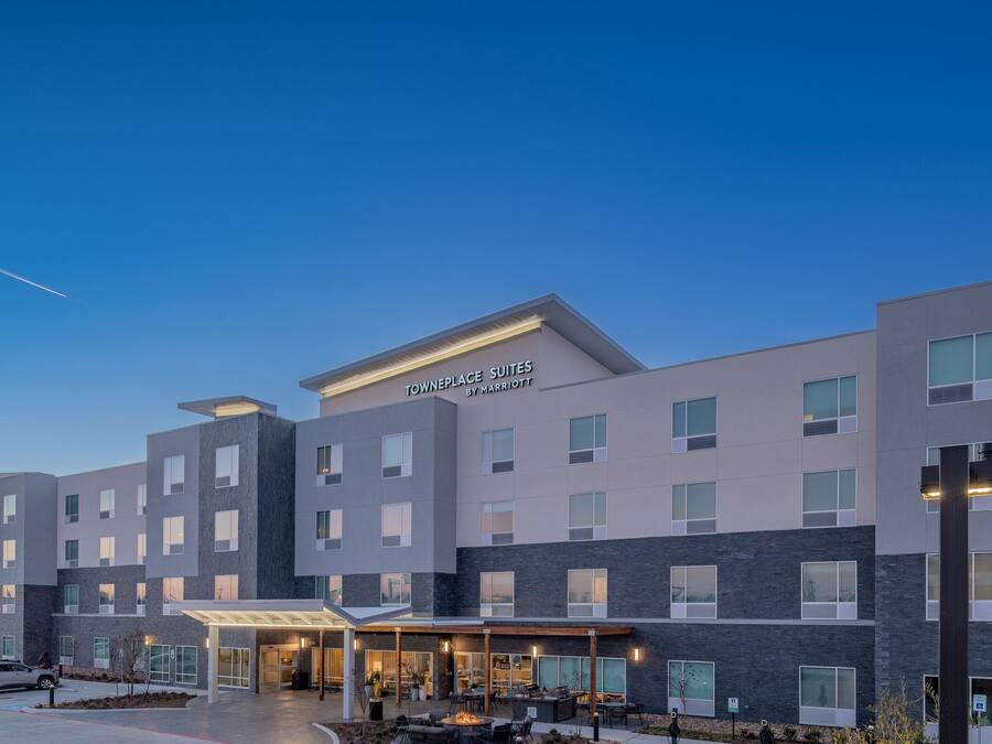 A modern hotel with a sign reading "TOWNPLACE SUITES BY MARRIOTT" and a covered outdoor seating area.