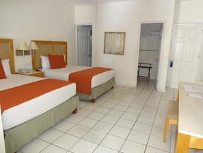 Ein Hotelzimmer mit zwei Betten, einem Schreibtisch, einem Stuhl, einem Telefon und einer Tür zu einem Badezimmer.