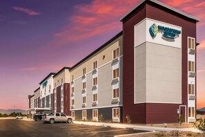 A multi-story hotel with a maroon and beige facade, a prominent logo, and a parking lot with several vehicles. - Woodspring Suites Tucson South (Tucson)