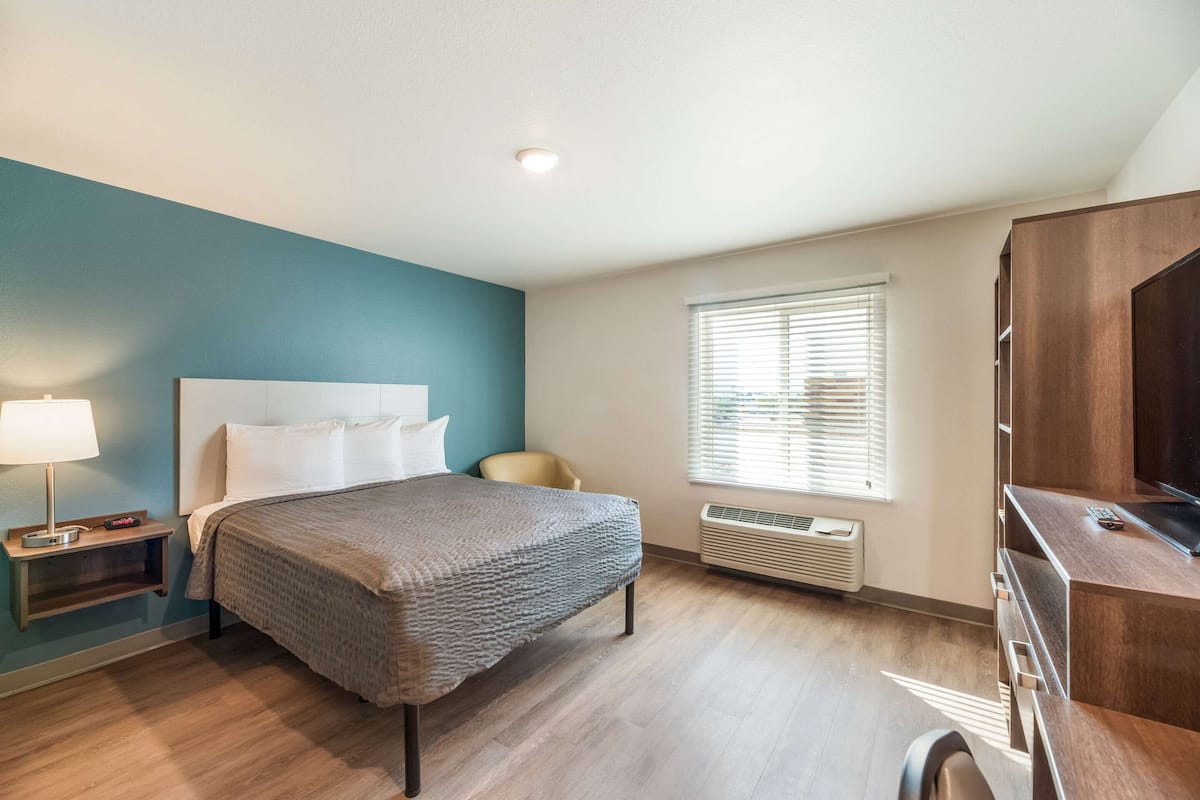 Habitación de hotel con cama, escritorio, silla, lámpara y ventana con persianas.