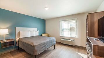 A hotel room with a bed, a desk, a chair, a lamp, and a window with blinds.