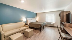 A compact hotel room with a bed, a sofa, a desk, and a TV. - Woodspring Suites Tucson South (Tucson)