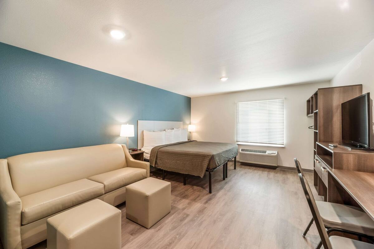Una habitación de hotel compacta con cama, sofá, escritorio y televisión.