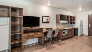 A modern kitchen with wooden cabinets, a built-in oven, a microwave, and a large flat-screen TV. - Woodspring Suites Tucson South (Tucson)
