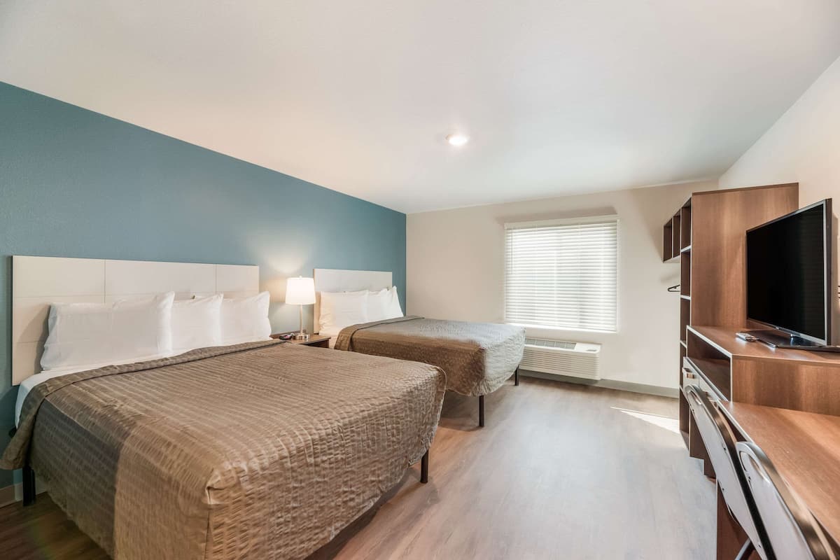 Habitación de hotel con dos camas, televisión y escritorio.