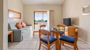 Quarto de hotel compacto com sofá, mesa de jantar de vidro e televisão.