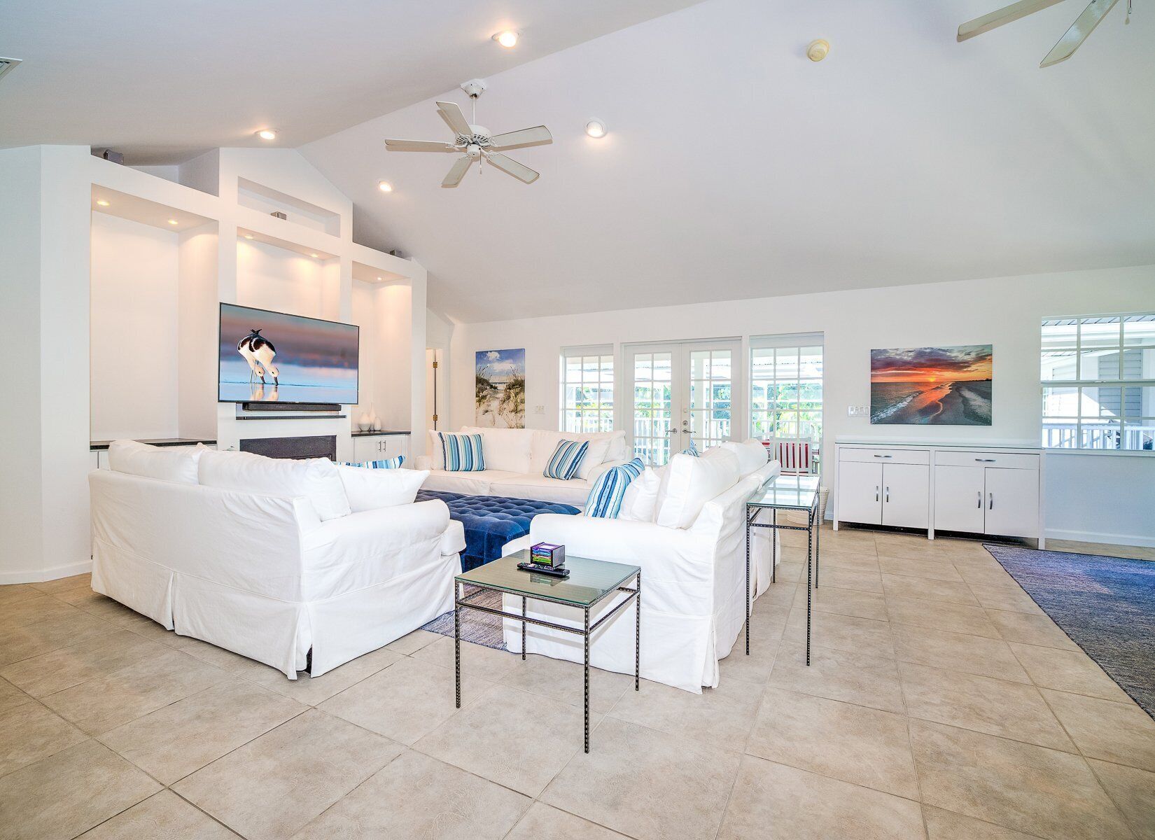 A spacious living room with white sofas, a glass coffee table, and artwork on the walls.