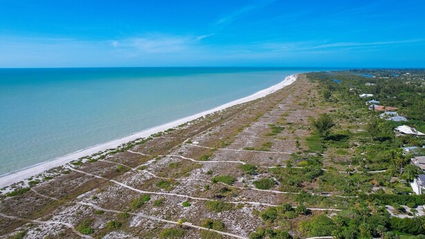 An aerial view of a coastal area with a sandy beach, green vegetation, and scattered buildings. - Spacious Single Family Home "Breaking Away" Steps from the Beach (Sanibel)