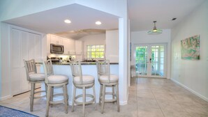 A modern kitchen with white cabinets, a microwave, and a bar area with four stools. - Spacious Single Family Home "Breaking Away" Steps from the Beach (Sanibel)