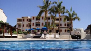 Un hotel con piscina, palme e zone relax all'aperto.