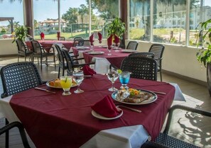 Zona pranzo all'aperto con tavoli apparecchiati per due, coperte rosse e sedie in vimini.