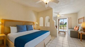 A hotel room with a large bed, a ceiling fan, a small table with a lamp, and a view of the outside balcony. - Elegant 2BR Condo for Friends (San José del Cabo)