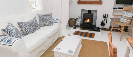 A white living room with a sofa, a coffee table, a fireplace, and a television.