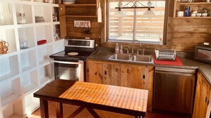 A compact kitchen with wooden cabinets, a built-in oven, a sink, and a window with blinds. - Good Place Farms Upper Barn (Lexington)