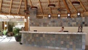 Una zona de recepción con un mostrador de piedra, techo de paja y un reloj en la pared.