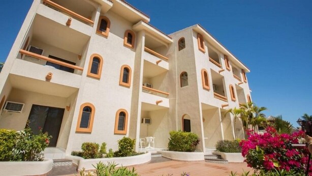 Un hotel de varios pisos con balcones, un patio empedrado y exuberante jardinería.