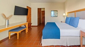 Una camera d'hotel con un letto, una TV fissata al muro, una scrivania con una sedia e una porta che dà su un'altra stanza.