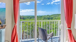 Un balcone con vista su una foresta e l'oceano, una sedia e tende rosse.