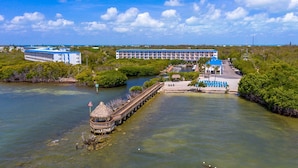 Un hotel sul lungomare con un molo che si protende sull'acqua, circondato da una vegetazione rigogliosa e cieli sereni.