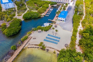Eine Vogelperspektive eines Resorts mit einer Marina, einem Strandbereich mit Liegestühlen und üppiger Vegetation.