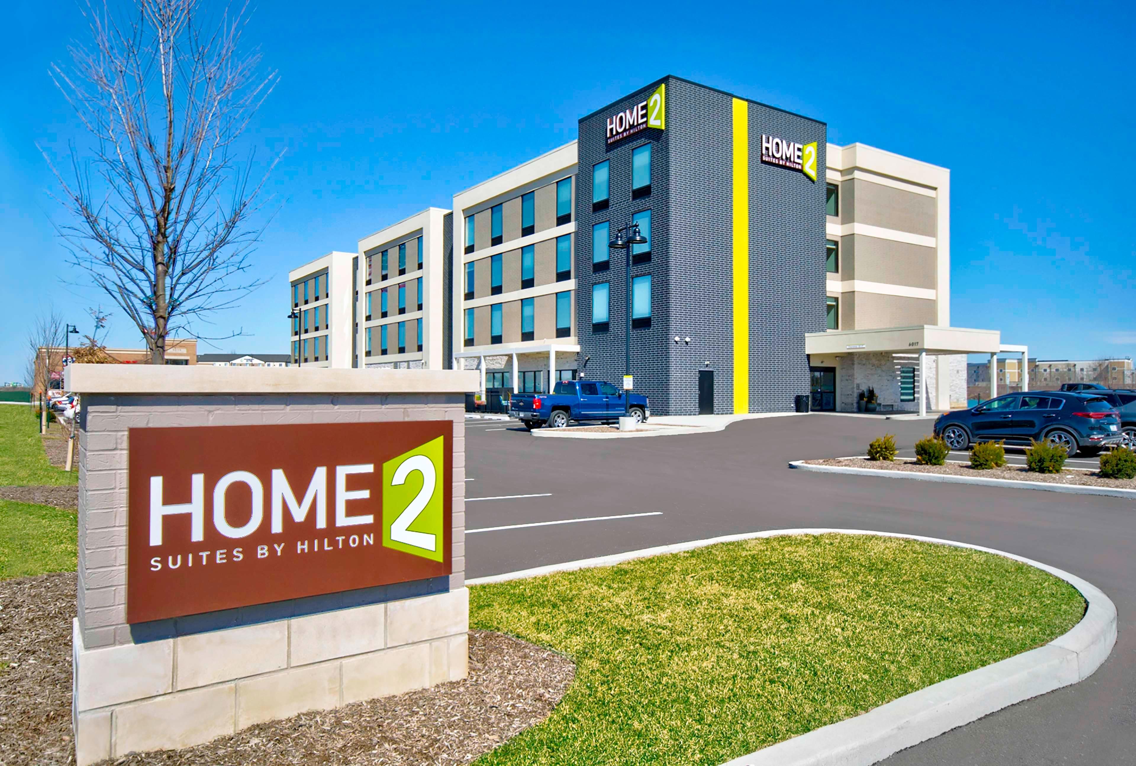 A modern hotel building with a sign reading "HOME 2 Suites by Hilton".