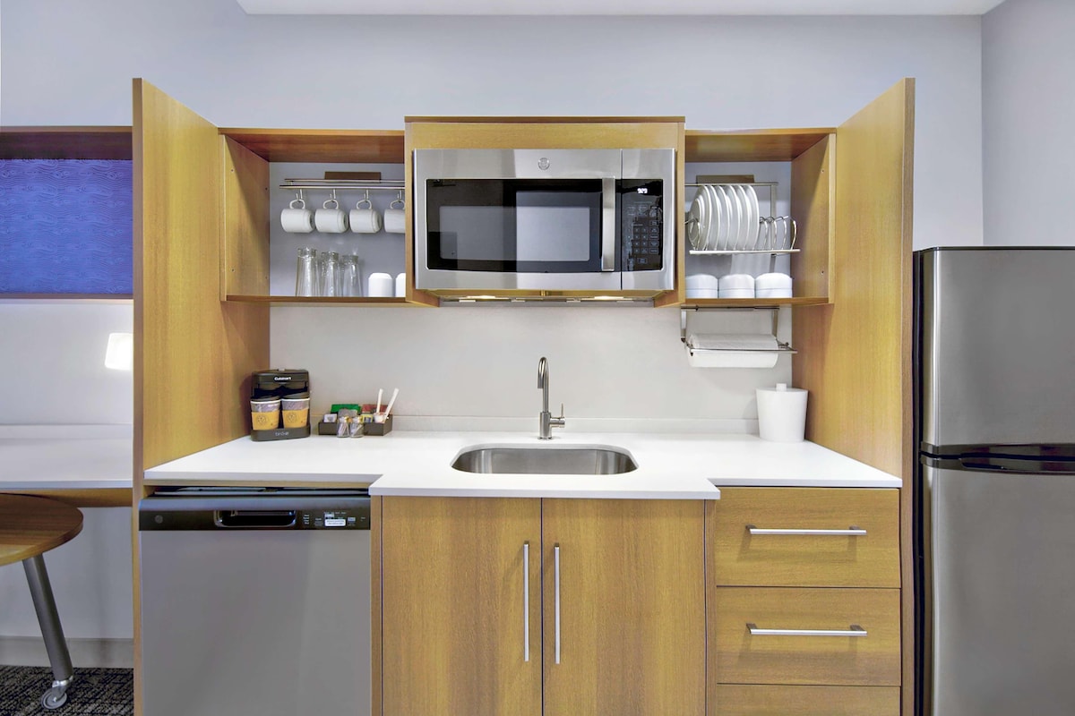 Una cucina compatta con forno a microonde integrato, lavello in acciaio inossidabile e pensili in legno.