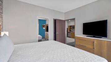 Ein Hotelzimmer mit einem großen Bett, einem Fernseher, einem Kleiderschrank und einer Küchenzeile im Hintergrund.