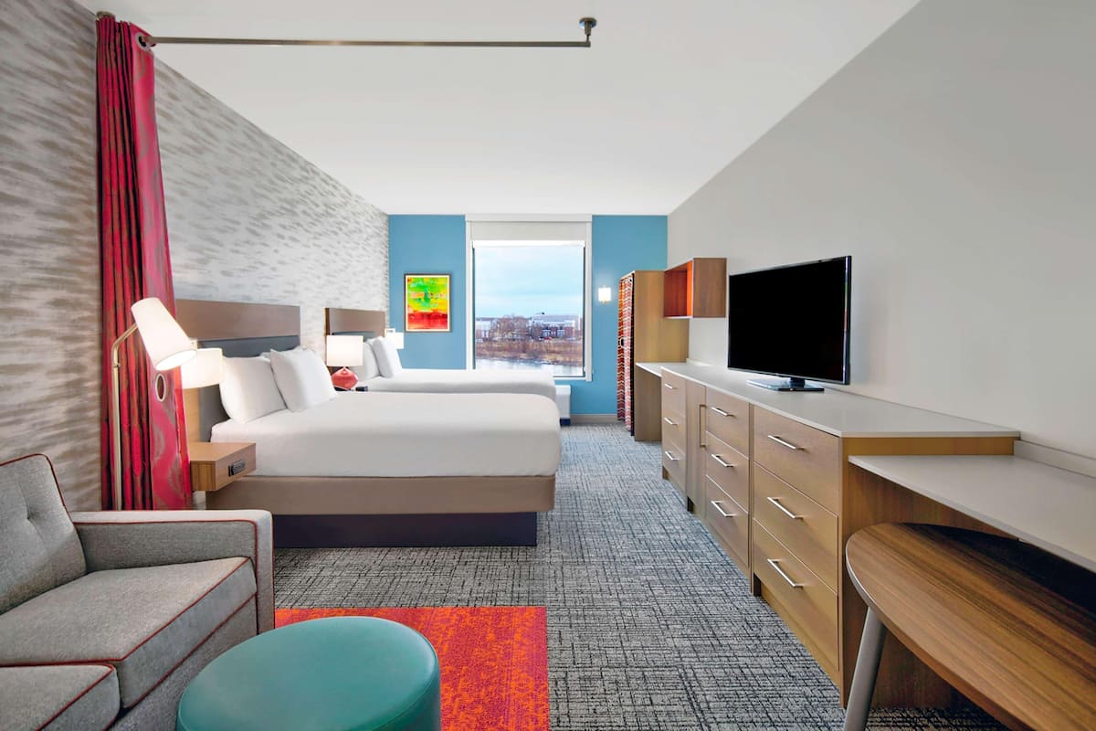 Une chambre d’hôtel équipée d’un lit, d’un bureau, d’une télévision, d’une chaise et d’une fenêtre donnant sur la ville.