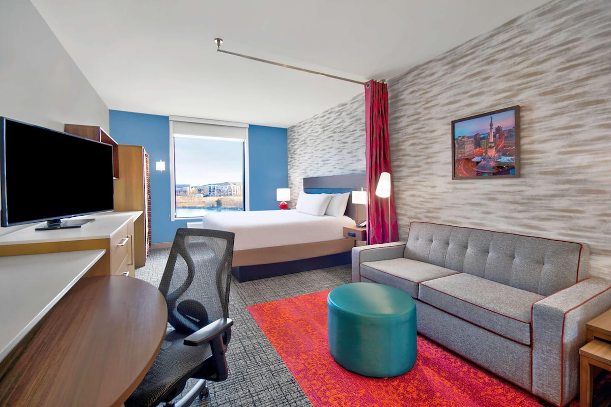 Une chambre d’hôtel équipée d’un lit, d’un canapé, d’une télévision, d’un bureau et d’une fenêtre donnant sur la ville.