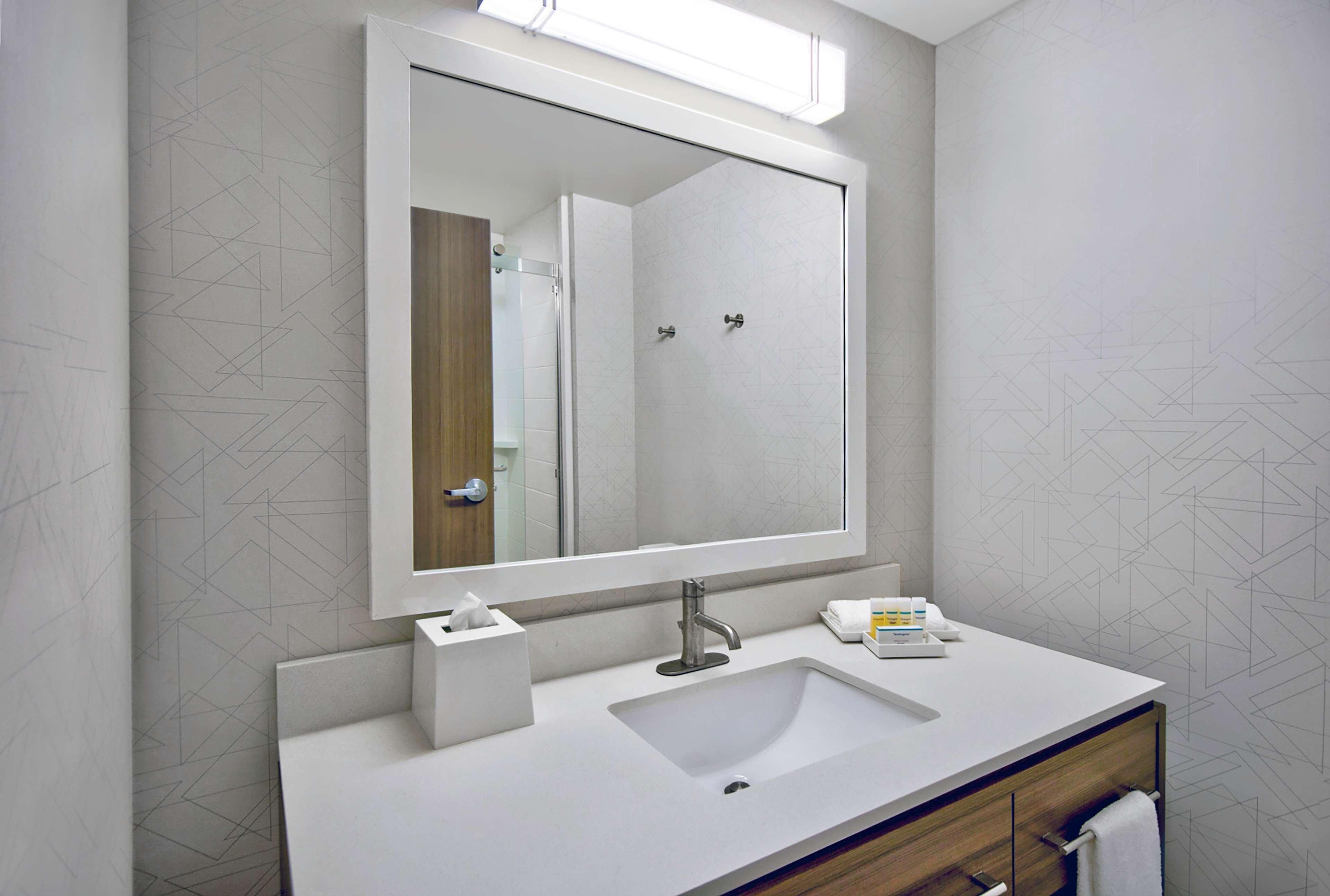 Une salle de bain moderne avec un grand miroir, un lavabo blanc et un meuble-lavabo en bois.