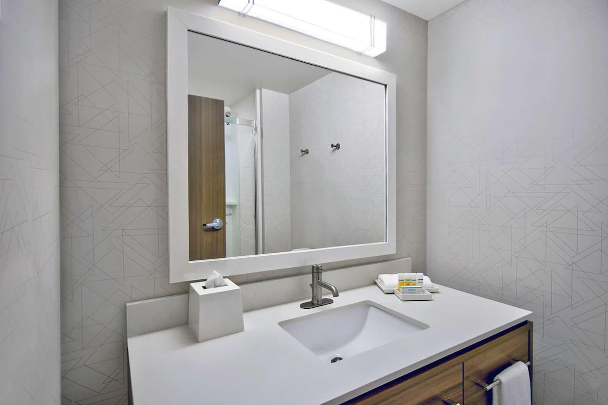 Une salle de bain moderne avec un grand miroir, un lavabo blanc et un meuble-lavabo en bois.