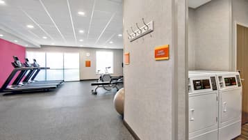 A gym with treadmills, a stationary bike, and a rowing machine. There is a sign for guest laundry and a wall-mounted towel rack.