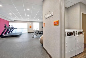 A gym with treadmills, a stationary bike, and a rowing machine. There is a sign for guest laundry and a wall-mounted towel rack. - Home2 Suites by Hilton Whitestown Indianapolis NW (Whitestown)