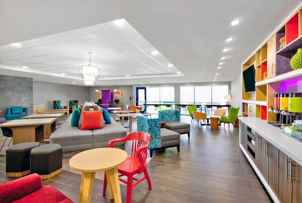 A modern lounge area with seating arrangements, a bar area, and a television screen. - Home2 Suites by Hilton Whitestown Indianapolis NW (Whitestown)