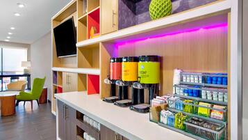 Un moderno vestíbulo de hotel con mostrador de recepción, máquinas de café y estanterías.