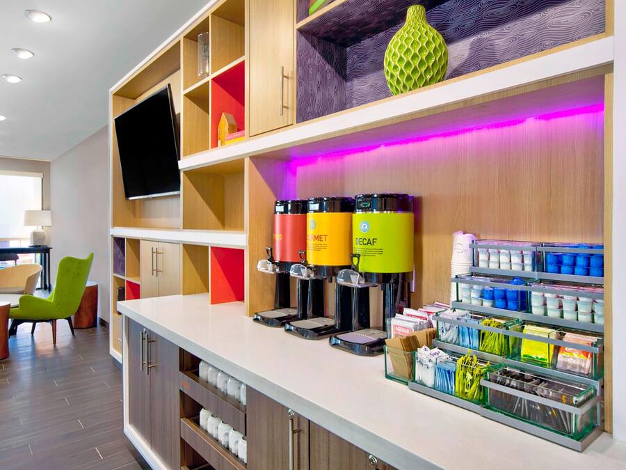 A modern hotel lobby with a reception desk, coffee machines, and storage shelves.