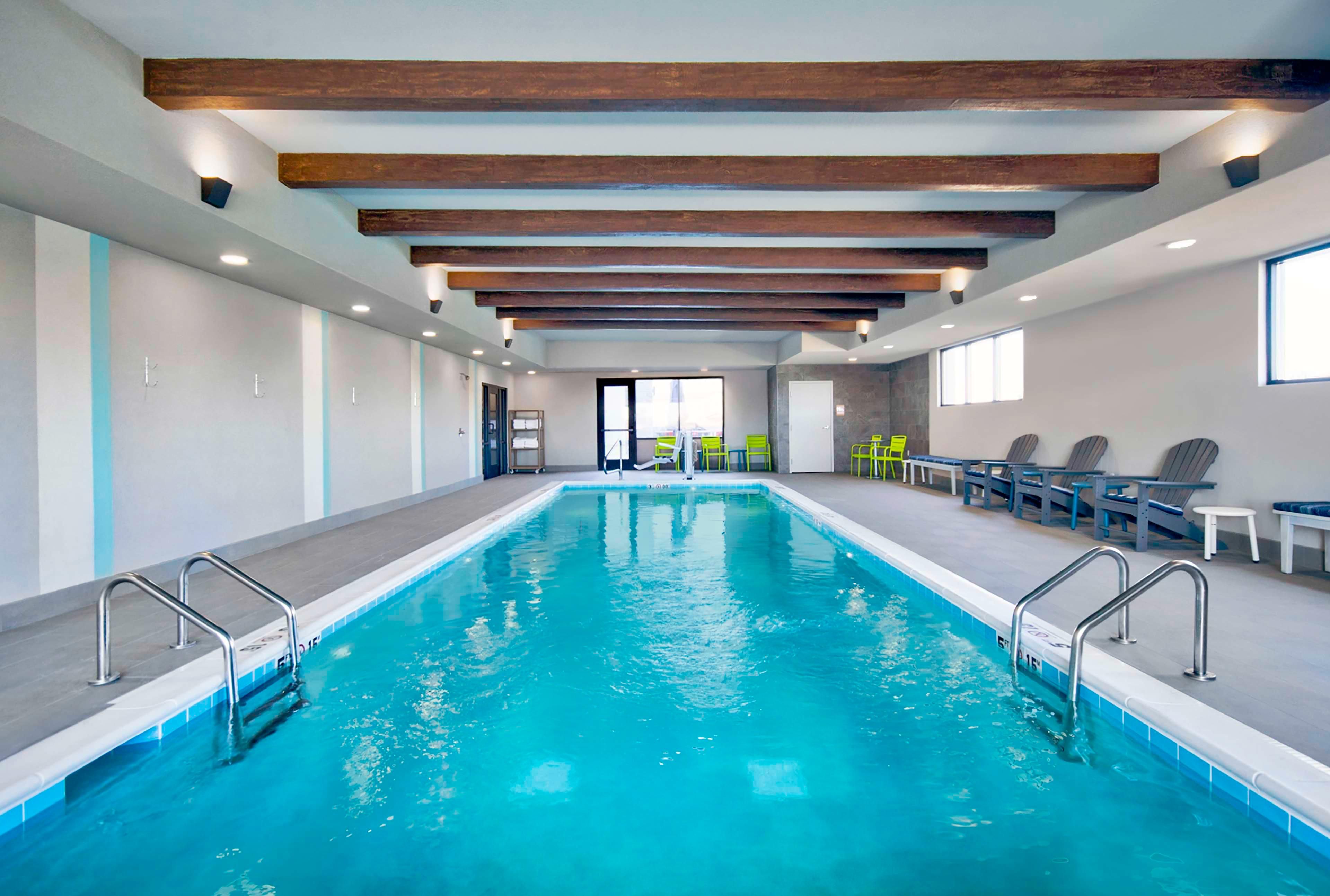 Una piscina con barandillas de metal, vigas de madera en el techo y sillas a un lado.