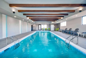 Una piscina con barandillas de metal, vigas de madera en el techo y sillas a un lado.
