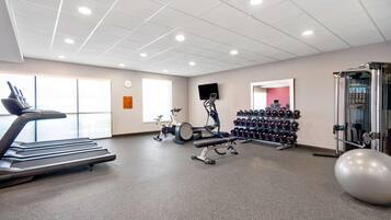 Une salle de sport équipée de tapis de course, de vélos d’exercice, d’haltères et d’un grand ballon de gymnastique.