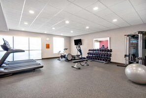 Een sportschool met loopbanden, trainingsfietsen, gewichten en een grote fitnessbal.