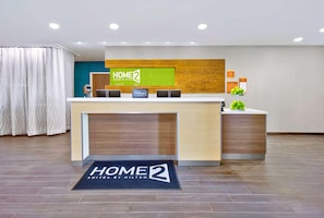 A reception desk with a 'HOME 2' sign, a digital screen, and a 'Hilton Honors' badge. - Home2 Suites by Hilton Whitestown Indianapolis NW (Whitestown)