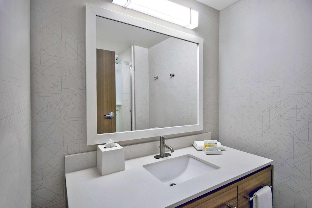 Un bagno moderno con uno specchio grande, un lavandino bianco e un mobile bagno in legno.