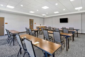 Une salle de conférence dotée de plusieurs tables et chaises, d’un téléviseur à écran plat fixé au mur et d’un revêtement de sol en moquette.